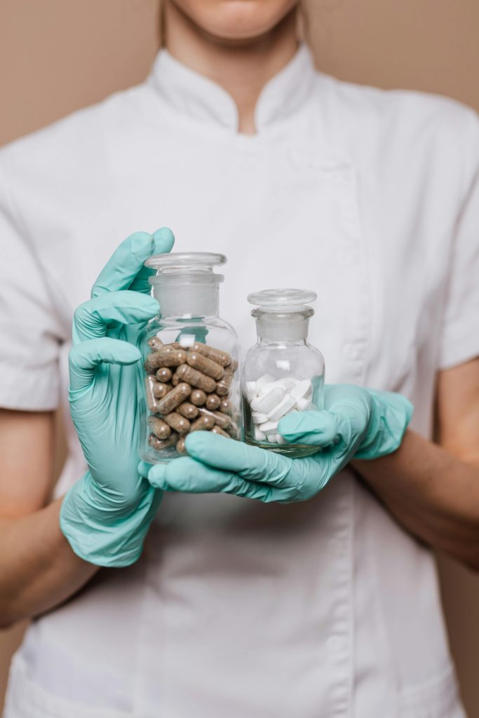 Ręce w turkusowych rękawiczkach trzymają dwie apteczne butelki z kapsułkami i tabletkami. Farmacja i medycyna.
