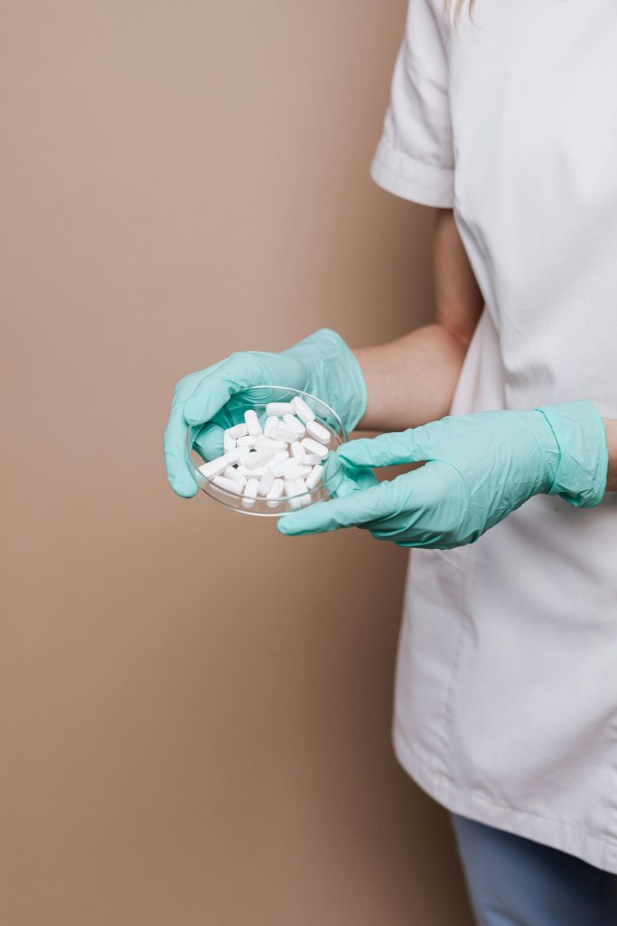 Osoba w rękawiczkach trzyma szalkę Petriego z białymi tabletkami. Koncept farmacji i laboratorium.